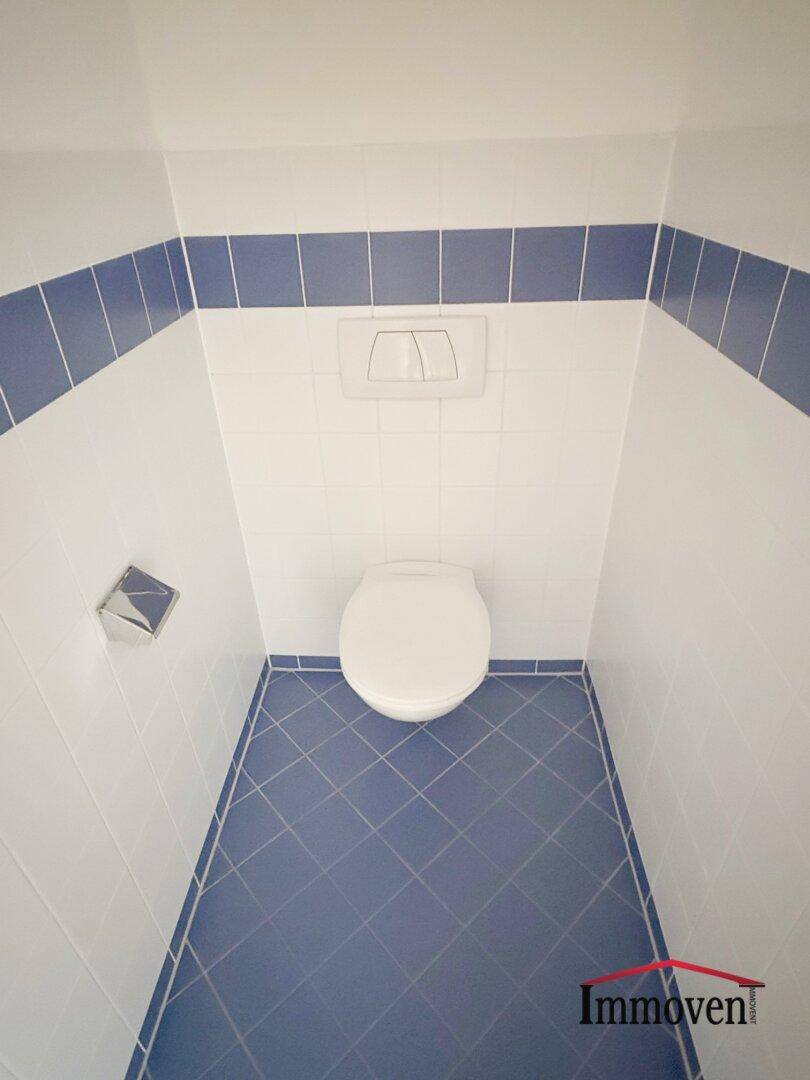 Separate Toilette mit blauen Bodenfliesen und weißer Wandverkleidung, sauber und funktional.