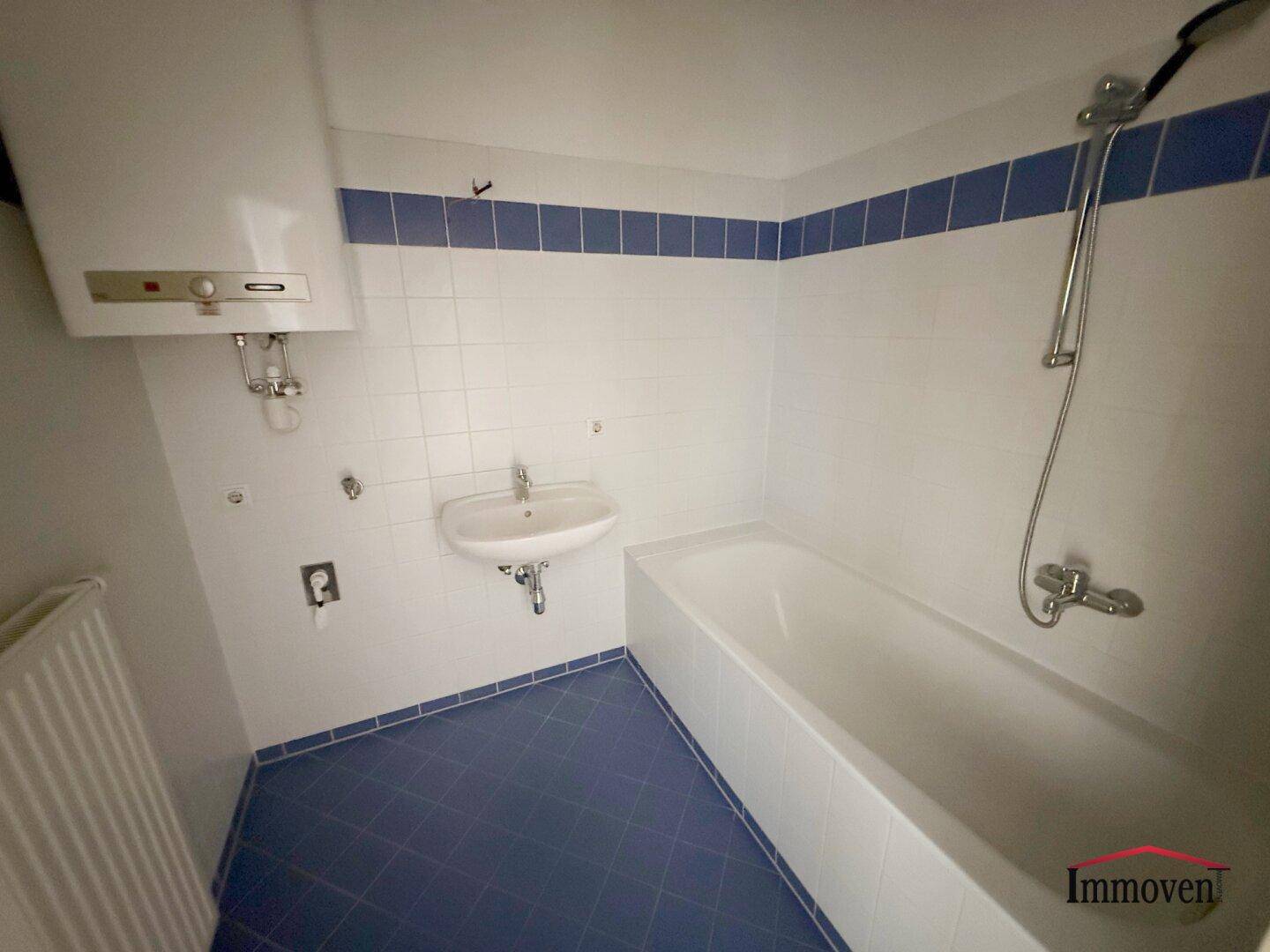 Badezimmer mit Badewanne, Waschbecken und blauen Fliesen, ausgestattet mit einem Warmwasserboiler.