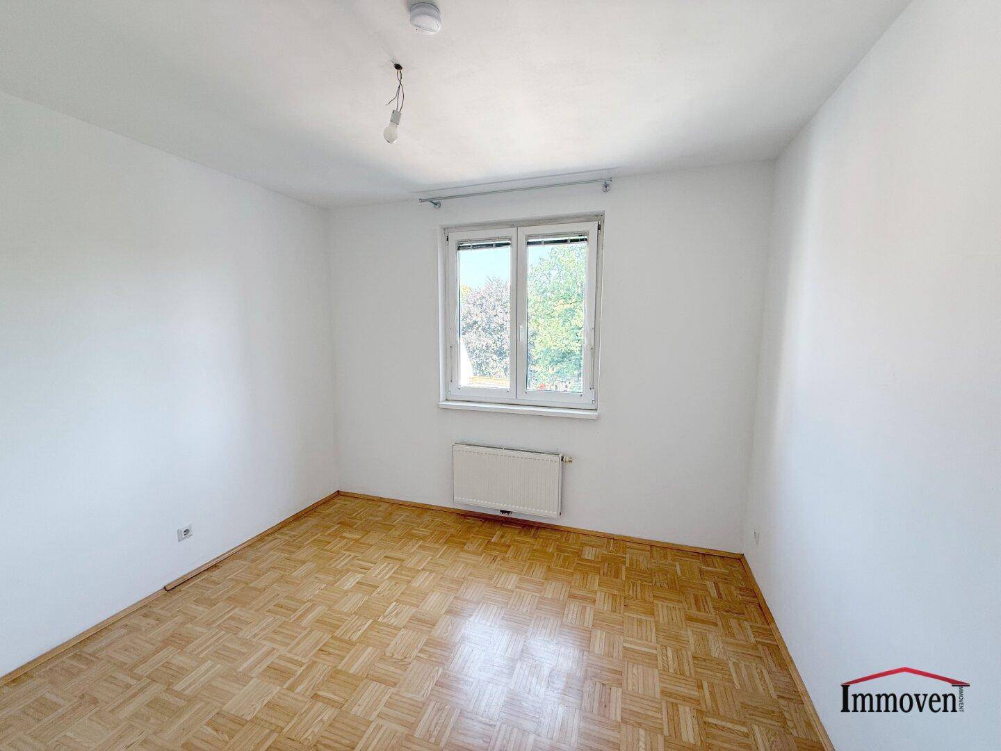 Geräumiges Zimmer mit Parkettboden und großem Fenster, das viel Tageslicht hereinlässt.
