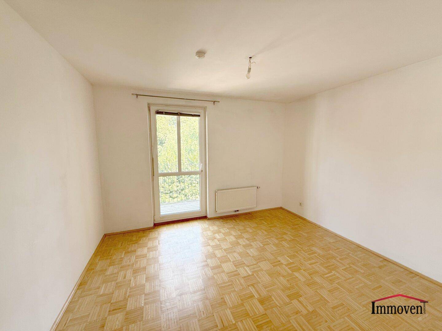 Helles Zimmer mit Parkettboden und Zugang zu einem französischen Balkon oder einer kleinen Loggia.