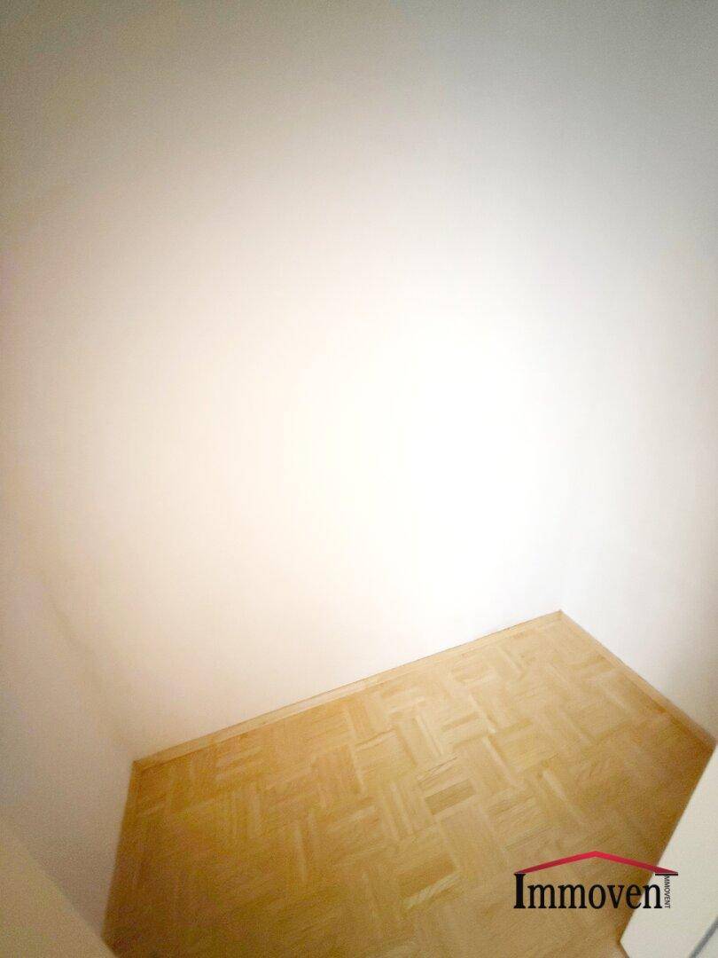 Ecke eines Raumes mit Parkettboden und hellen Wänden, die auf ein offenes Ambiente hindeuten.