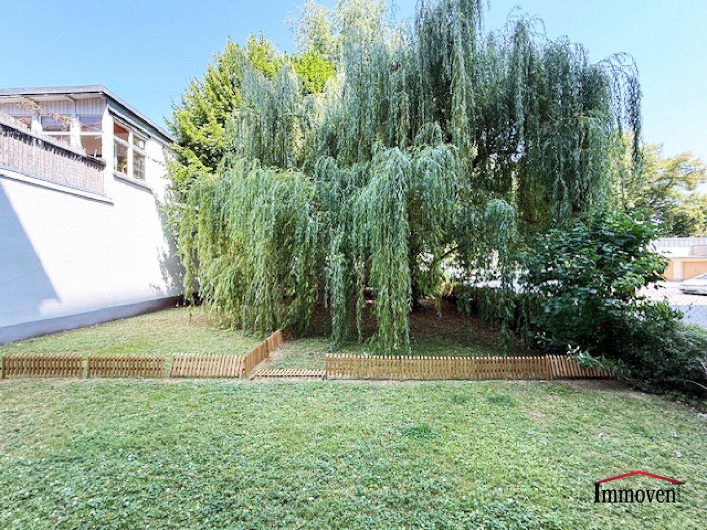 Gepflegter Garten mit Rasen, großen Weidenbäumen und einem kleinen Holzzaun.
