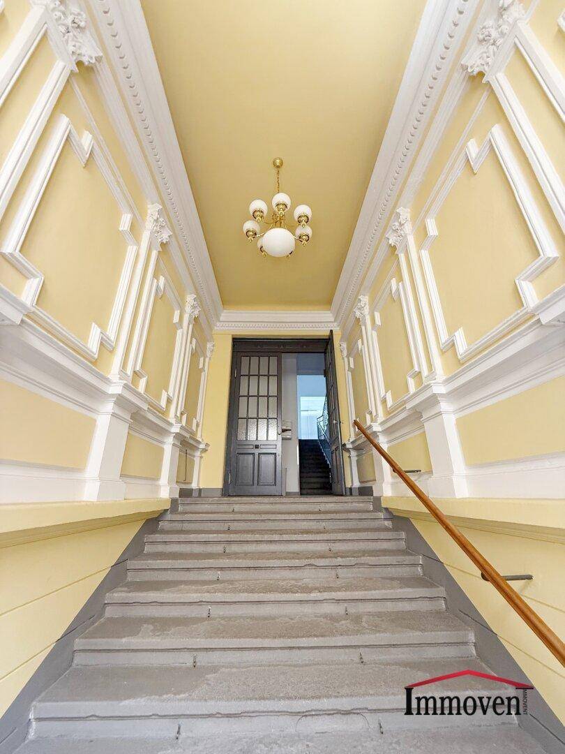 Elegantes Treppenhaus mit Stuckelementen und klassischem Kronleuchter, das den historischen Charme bewahrt.