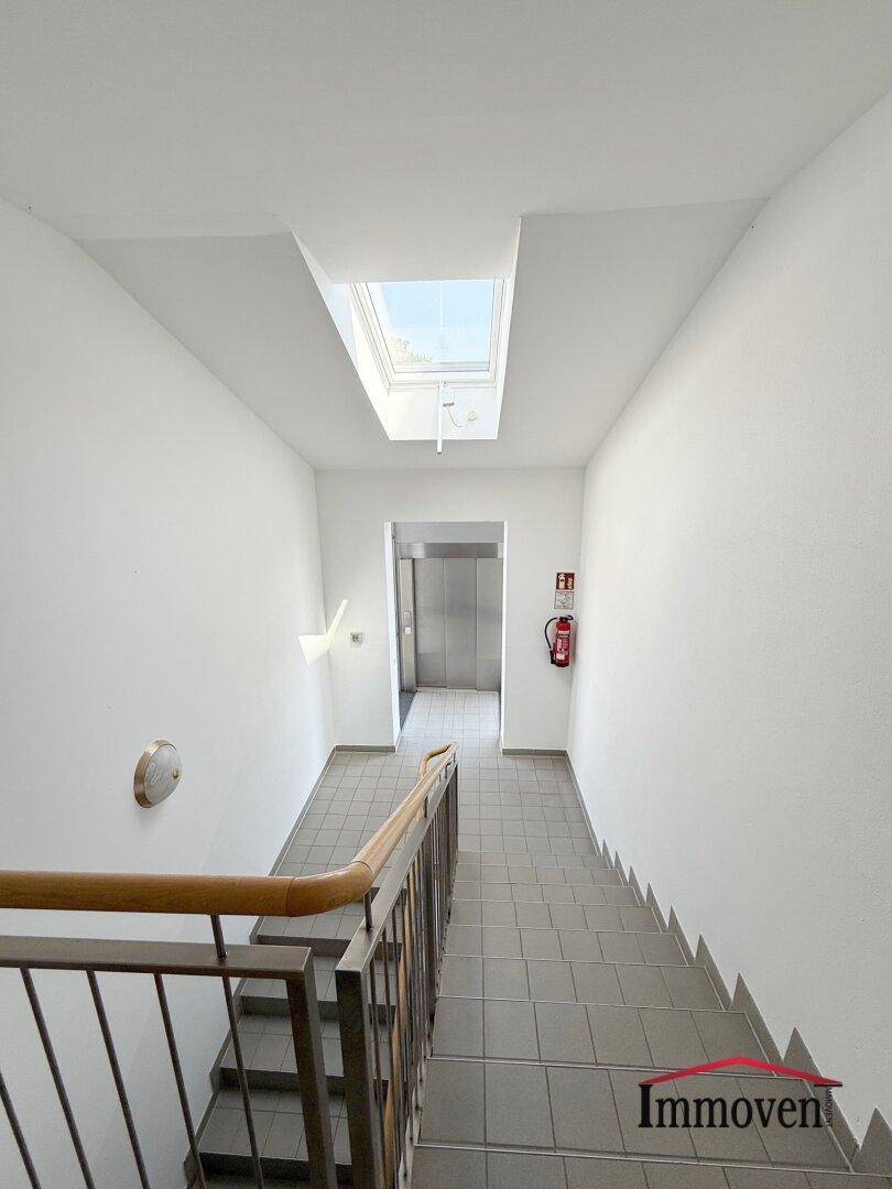 Modernes Treppenhaus mit Tageslicht durch ein Oberlicht und Zugang zum Aufzug.