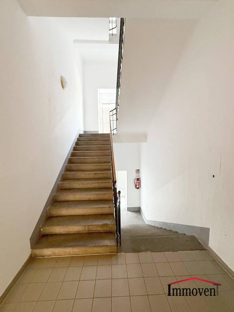 Helles Treppenhaus mit Fliesenboden und schlichtem Geländer, führt zu den oberen Etagen.