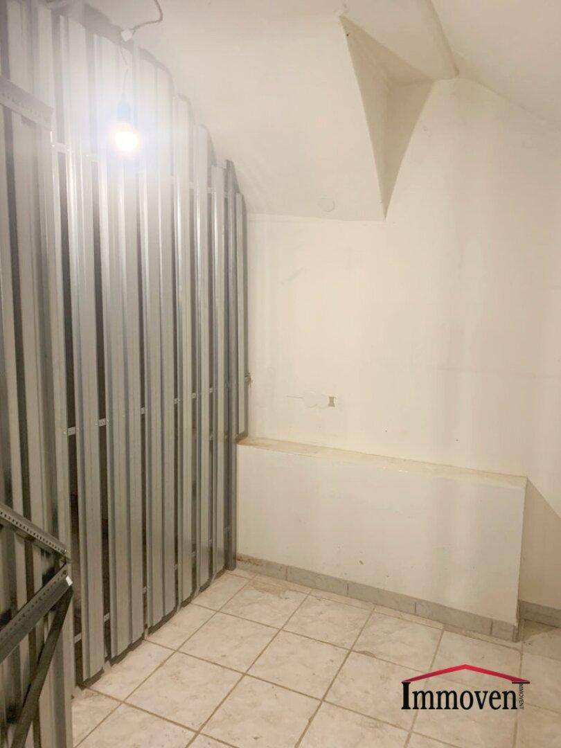 Blick in einen Kellerraum mit Metallabtrennungen für Lagerabteile und einem gefliesten Boden.