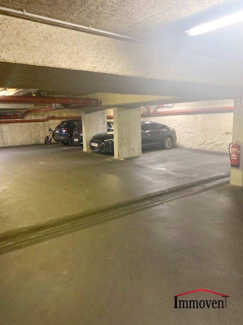 Tiefgarage mit geparkten Fahrzeugen, Betonstützen und sichtbaren Installationen an der Decke.