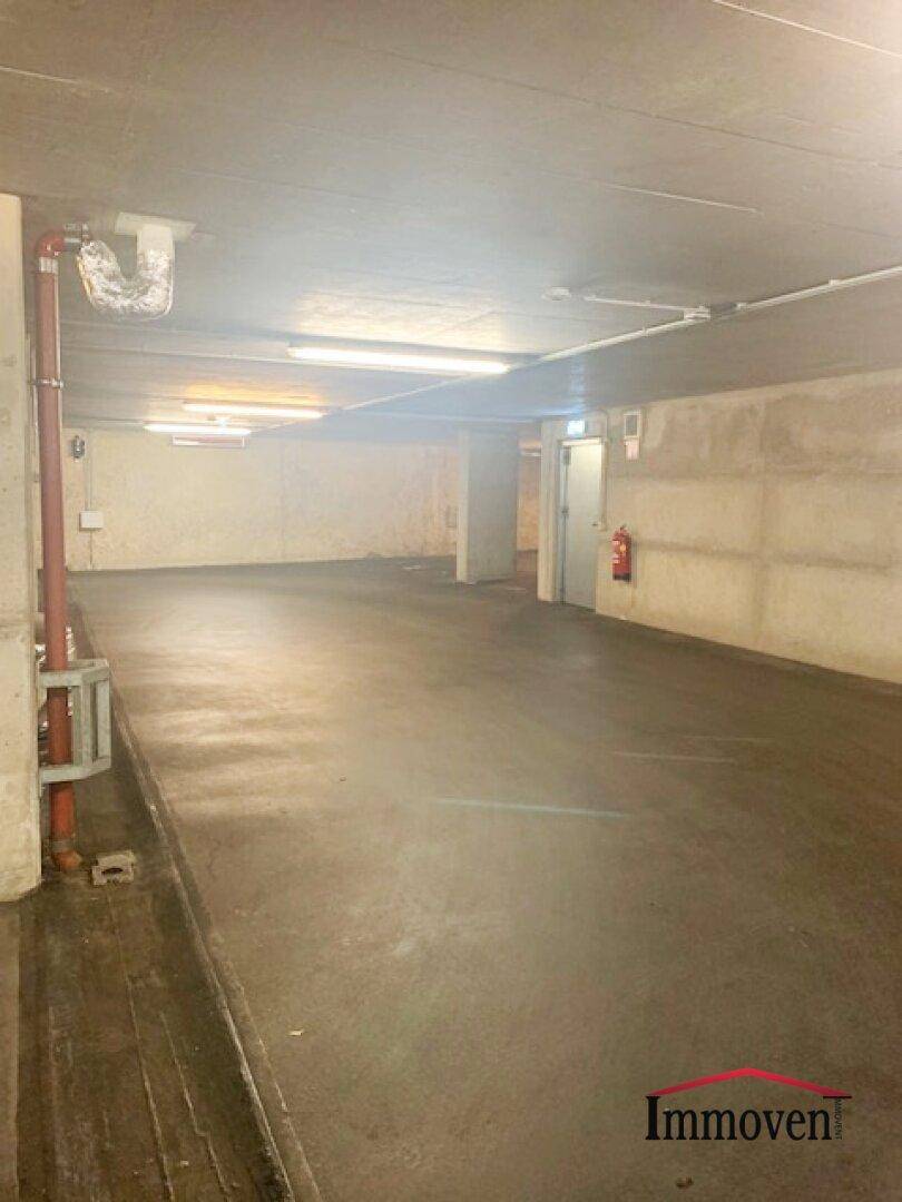Leerer Bereich einer Tiefgarage mit Betonwänden, Deckenbeleuchtung und einem Feuerlöscher an der Wand.