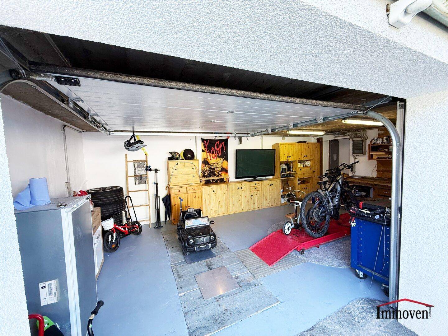 Geräumige Garage mit offenem Tor, ausgestattet als Werkstatt und Abstellbereich für Fahrzeuge.