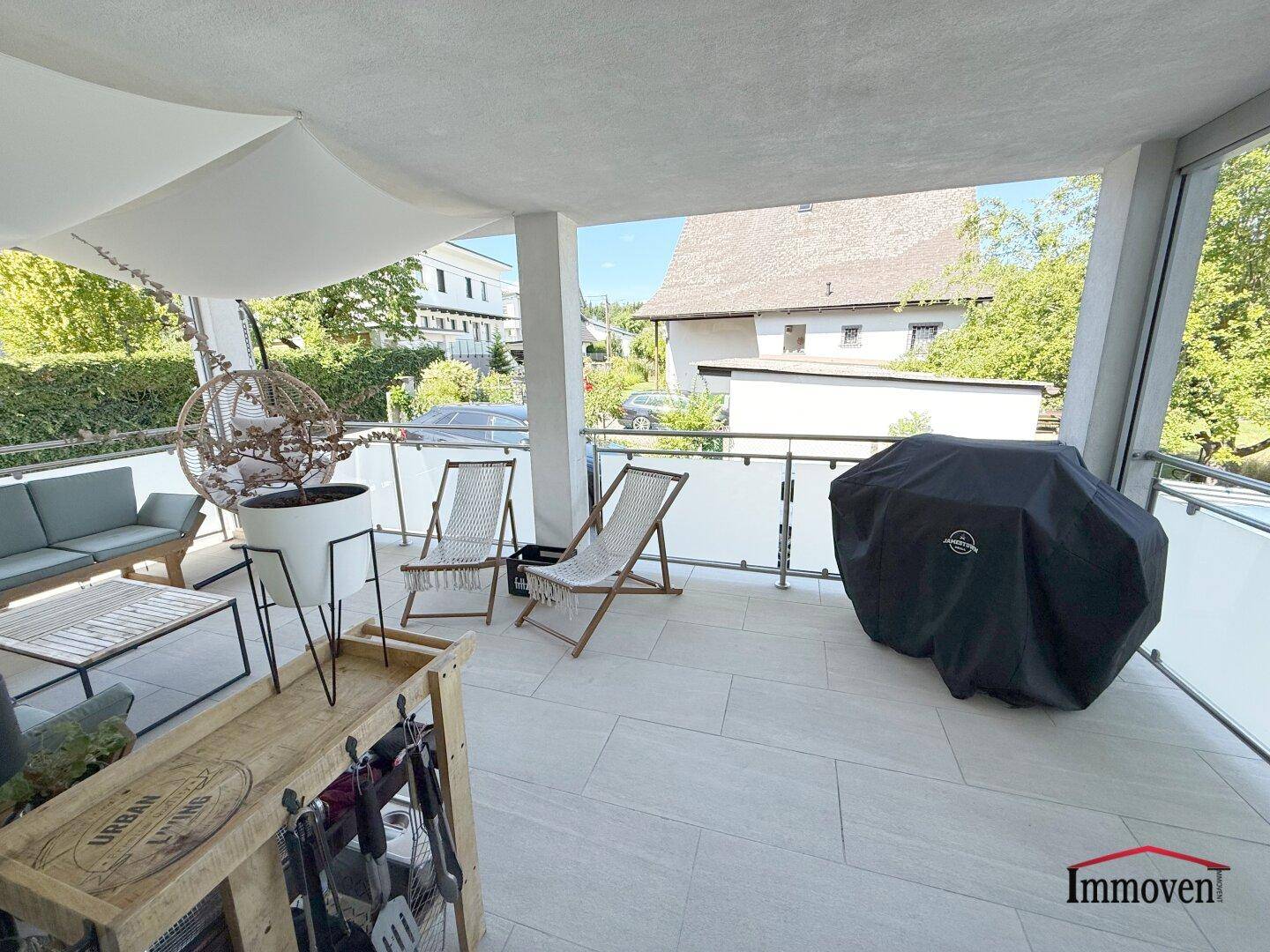 Großer überdachter Balkon mit Fliesenboden, Sitzgelegenheiten und Grill.