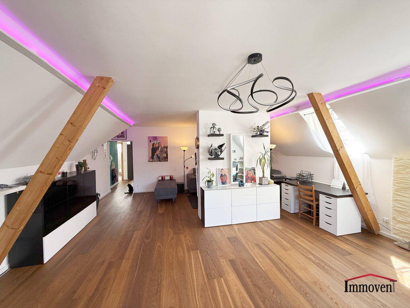Helles Dachgeschoss-Wohnzimmer mit Holzboden, Arbeitsbereich und modernen Möbeln.