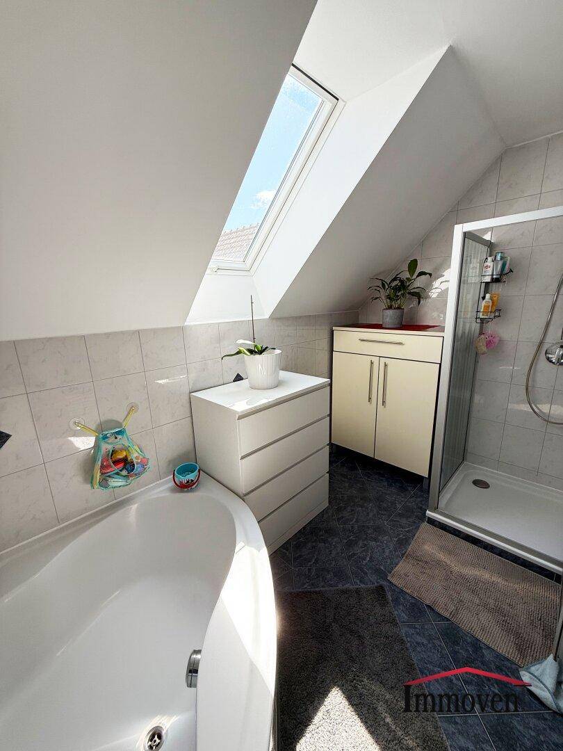Helles Badezimmer im Dachgeschoss mit Badewanne, Dusche und Dachfenster.