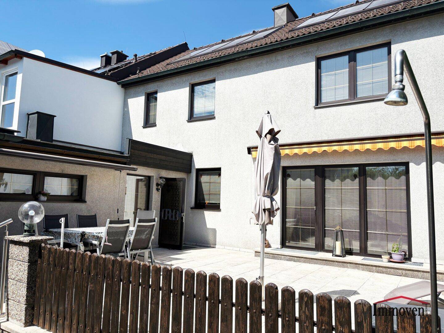Große gepflasterte Terrasse hinter dem Haus mit Esstisch, Sonnenschirm und Markise.