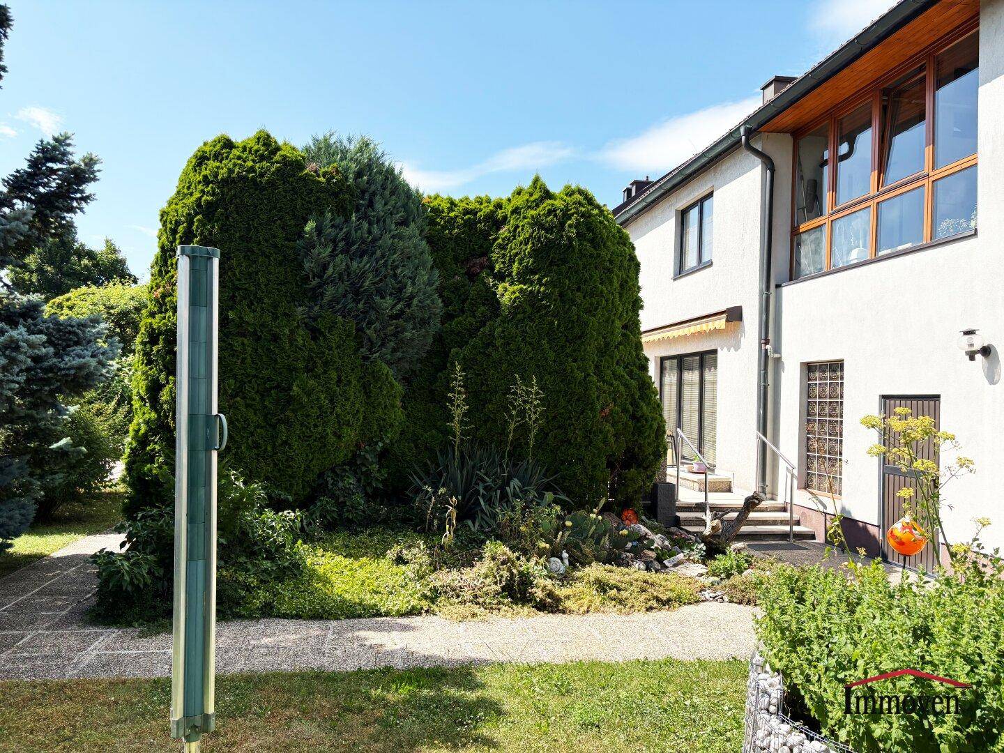 Seitlicher Gartenbereich des Hauses mit hohen Hecken und einem kleinen Kiesweg.