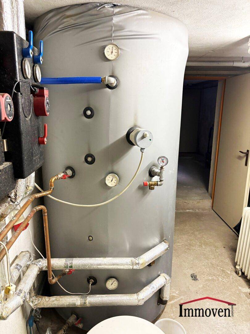 Heizungsraum mit großem Warmwasserspeicher und sichtbaren Rohrleitungen.