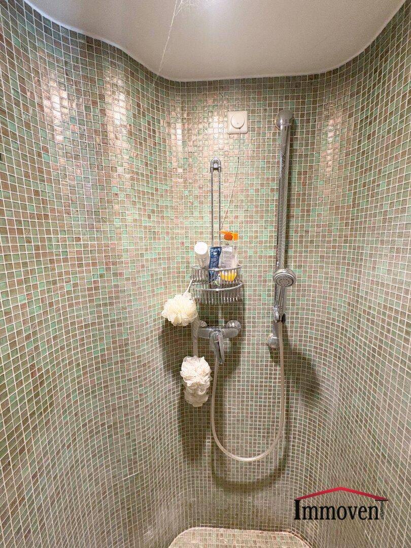 Duschbereich mit kleinen grünen Mosaikfliesen und Handbrause.