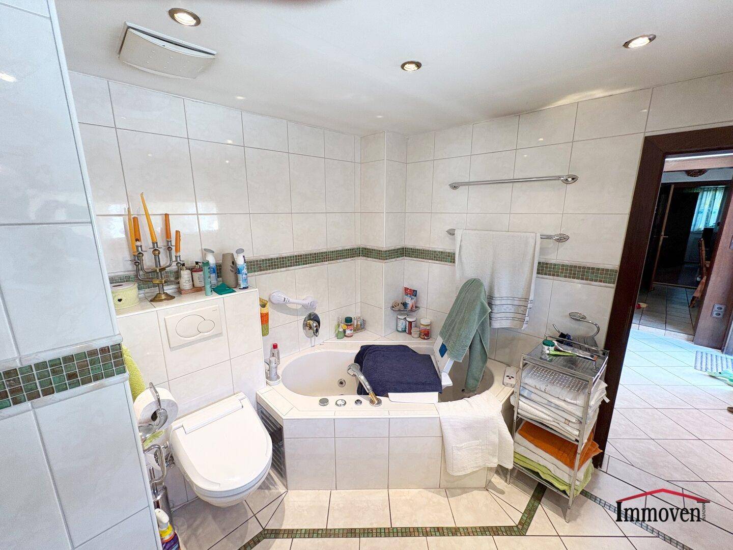 Badezimmer mit Eckbadewanne, WC und weißen Fliesen mit grüner Bordüre.