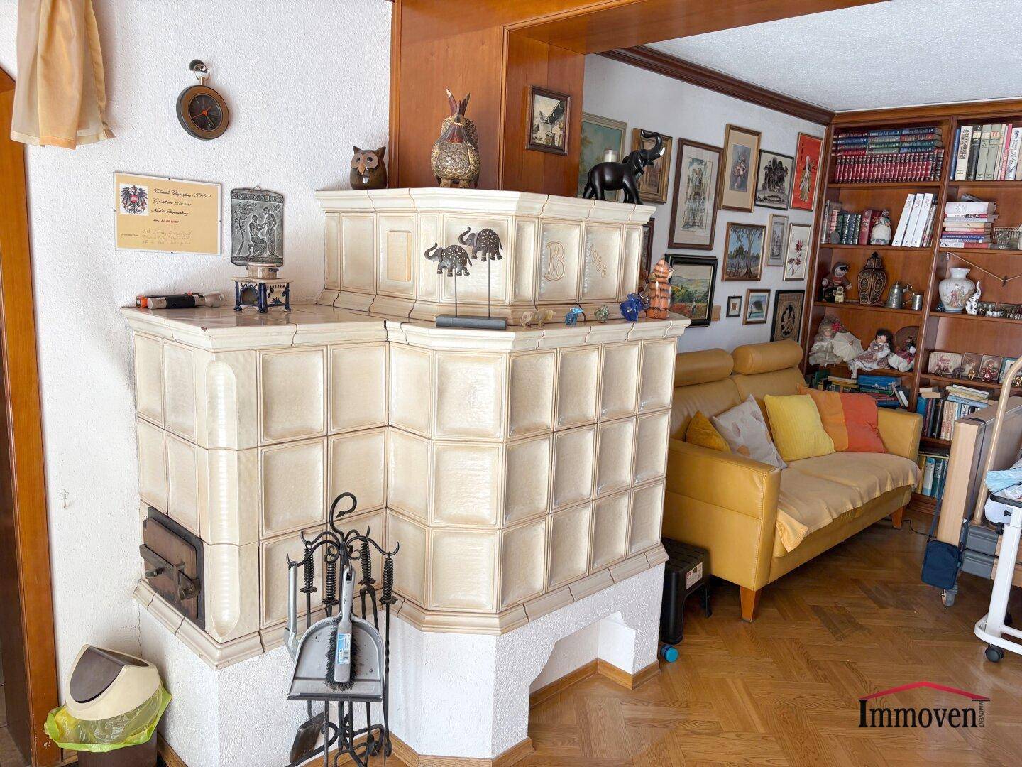 Wohnzimmer mit traditionellem Kachelofen, Parkettboden und gelbem Sofa.