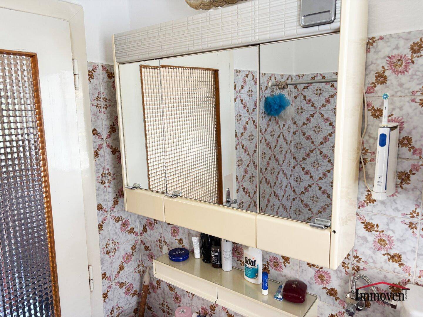 Badezimmer mit floraler Tapete, Spiegelschrank und Waschbecken.