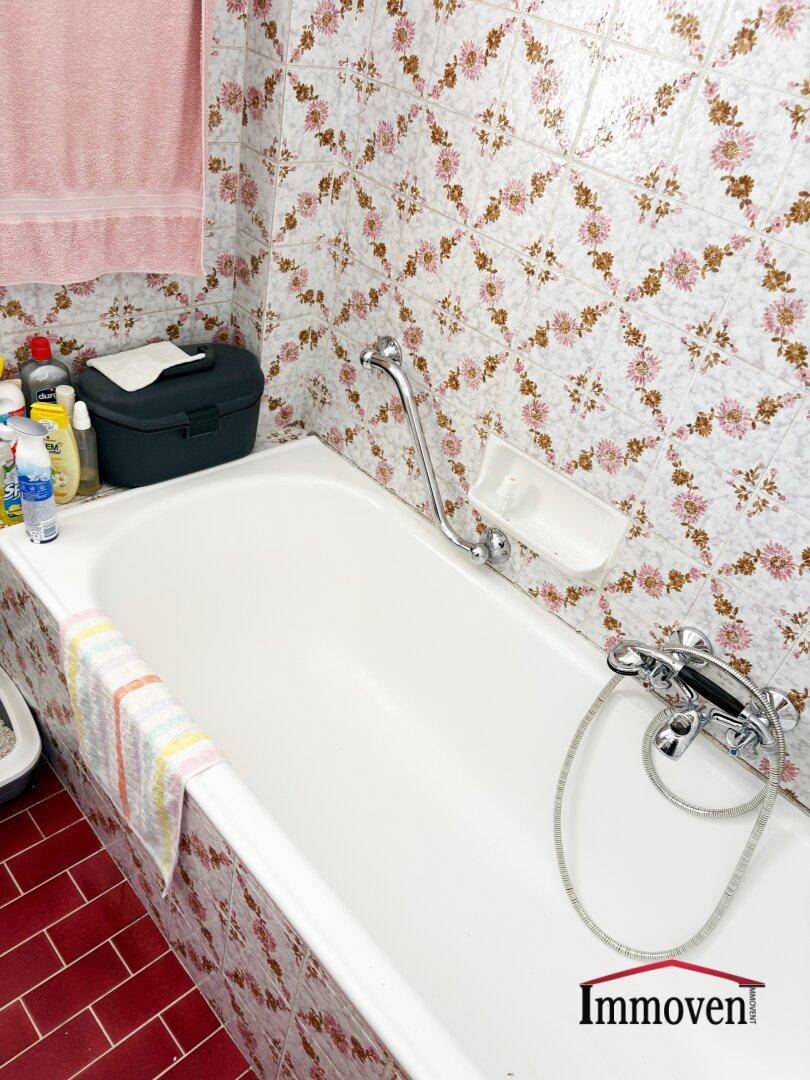 Badezimmer mit Badewanne und roten Fliesen, dekoriert mit floralen Mustern.