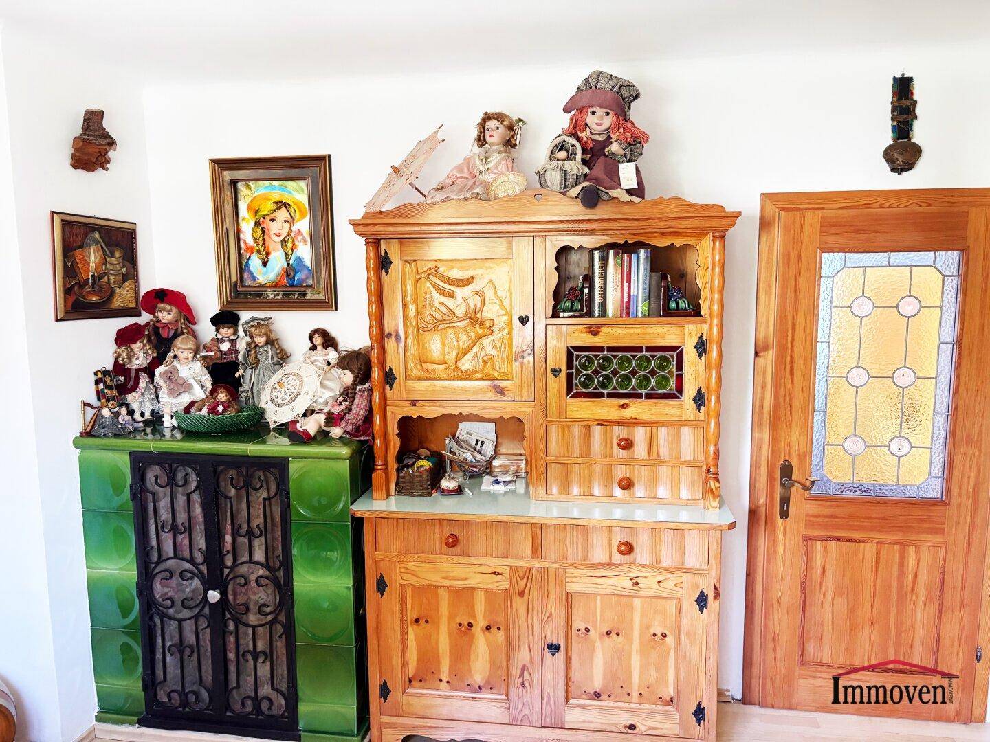 Traditioneller Kachelofen und ein verzierter Holzschrank mit Puppen und Dekorationen.