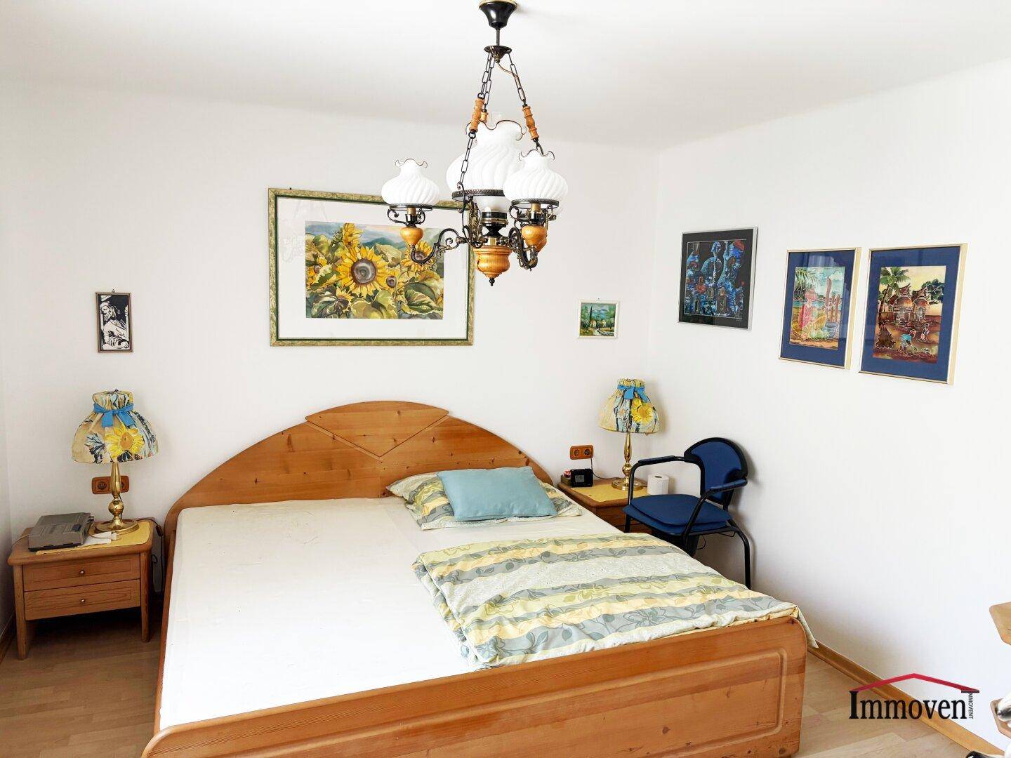 Schlafzimmer mit einem Holzbett, Nachttischen und gerahmten Bildern an den weißen Wänden.