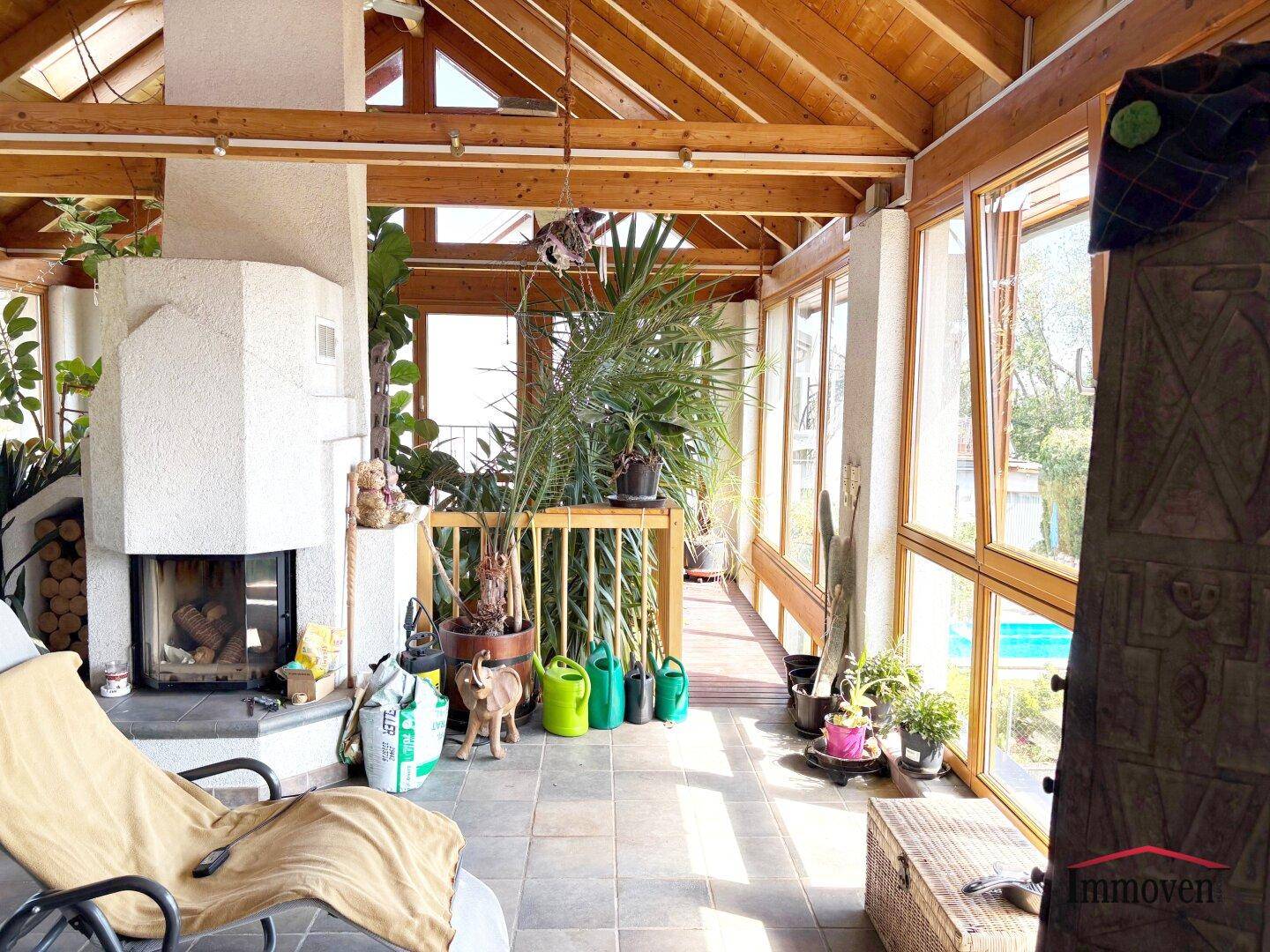 Heller Wintergarten mit Kamin, Fliesenboden und zahlreichen Pflanzen, ideal zum Entspannen.
