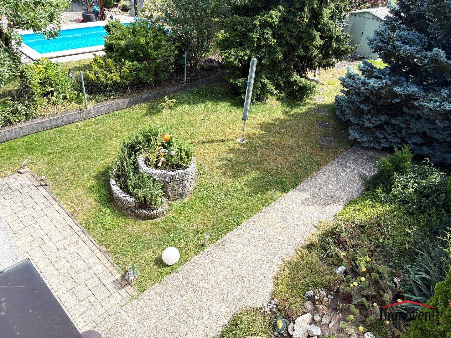 Gepflegter Garten mit Rasenfläche, Hochbeet und einem Swimmingpool im Hintergrund.