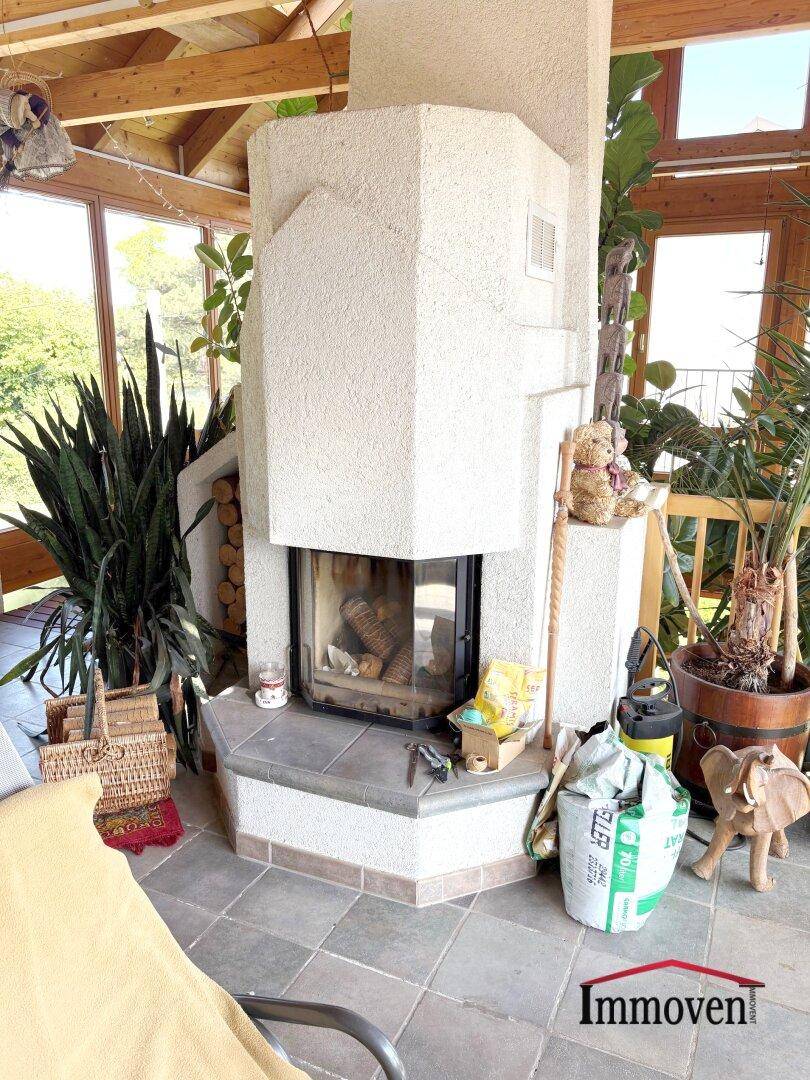 Gemütlicher Kamin im Wintergarten, umgeben von Grünpflanzen und einem Fliesenboden.