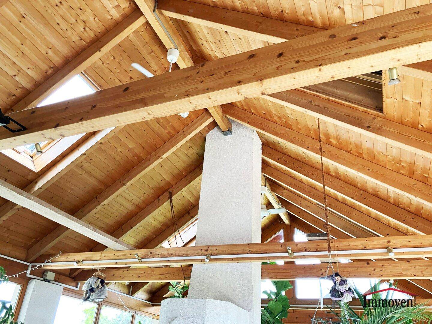 Hohe Holzdecke mit sichtbaren Balken und einem zentralen Kaminabzug im Wintergarten.