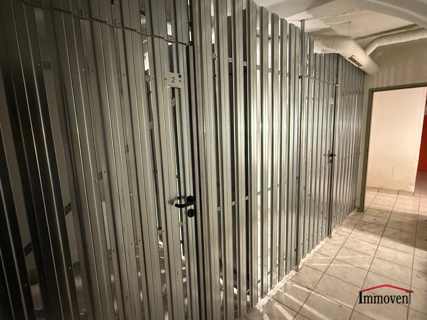 Reihen von Metall-Lagerabteilen in einem gut erhaltenen Kellerraum mit Fliesenboden und sichtbaren Lüftungsrohren.