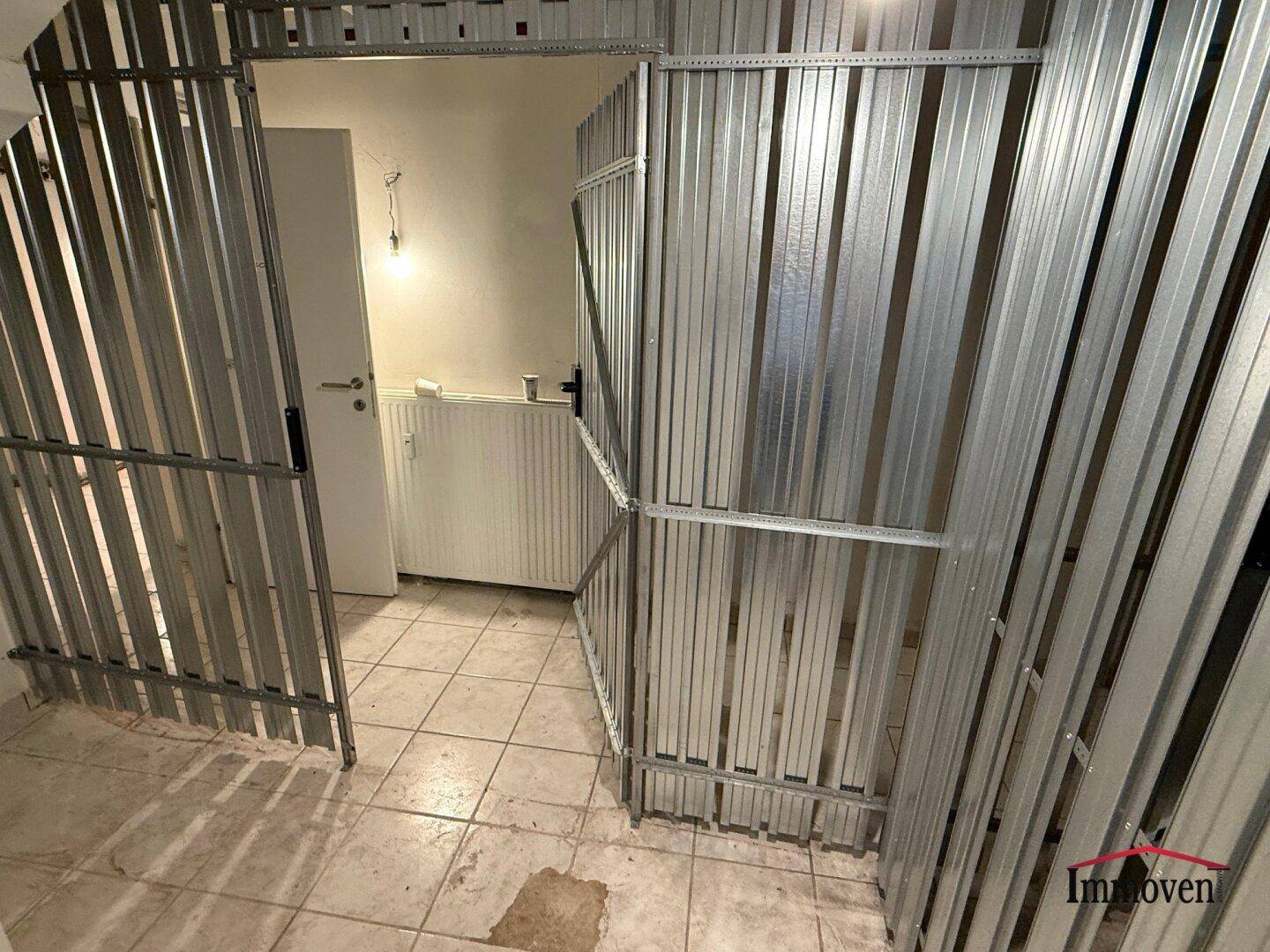 Offenes Metall-Lagerabteil in einem Kellerraum mit Heizkörper und Fliesenboden, bereit zur Nutzung.