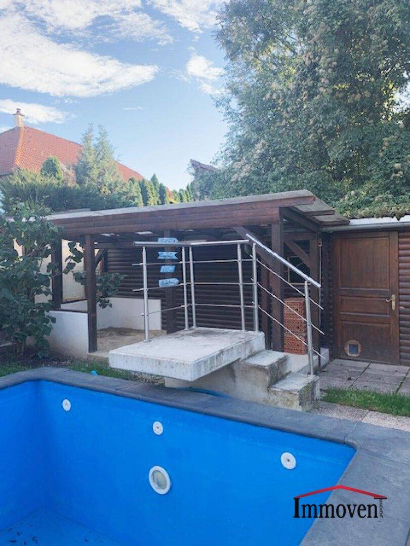 Poolbereich mit Einstiegstreppe und einem kleinen Holzhaus im Hintergrund.