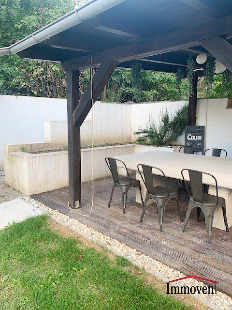 Gemütlicher überdachter Terrassenbereich mit Esstisch und Blick auf die Gartenbepflanzung.