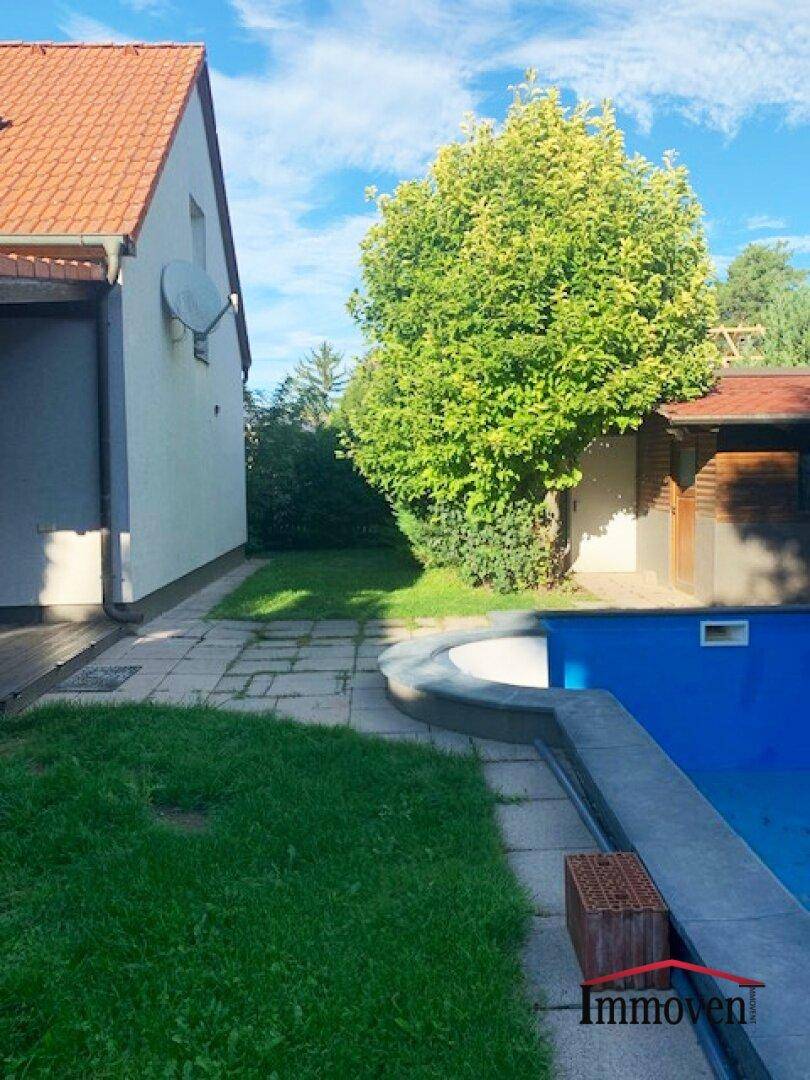 Seitenansicht des Hauses mit Poolbereich, Rasenfläche und Baumbestand.