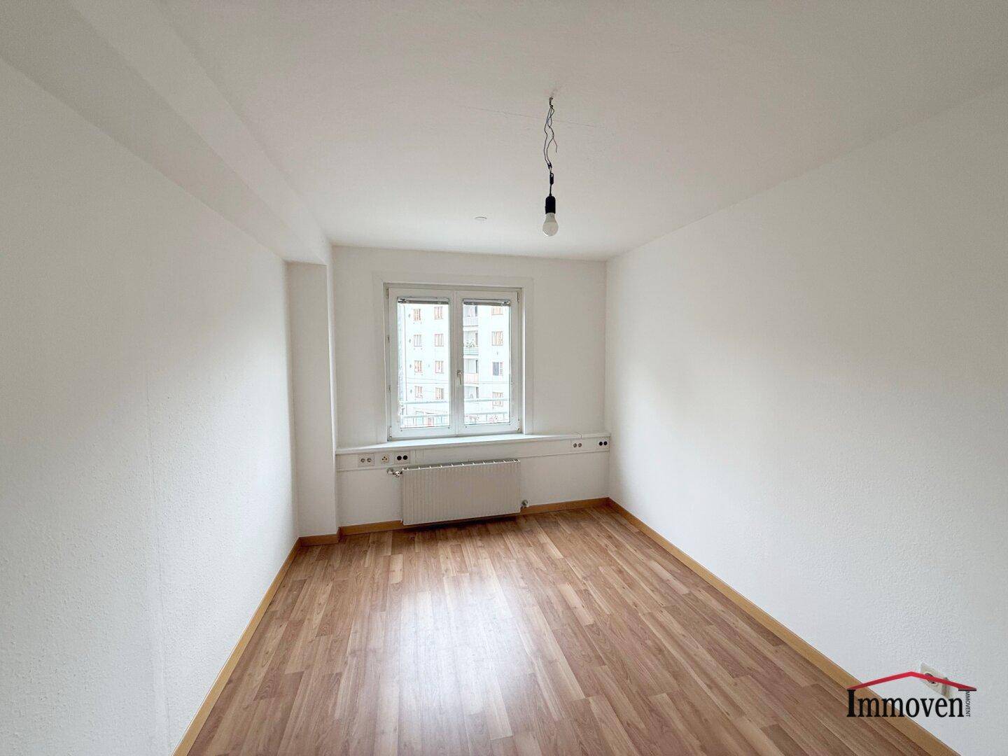 Leeres Zimmer mit Holzboden und einem Fenster, bereit zur individuellen Gestaltung.