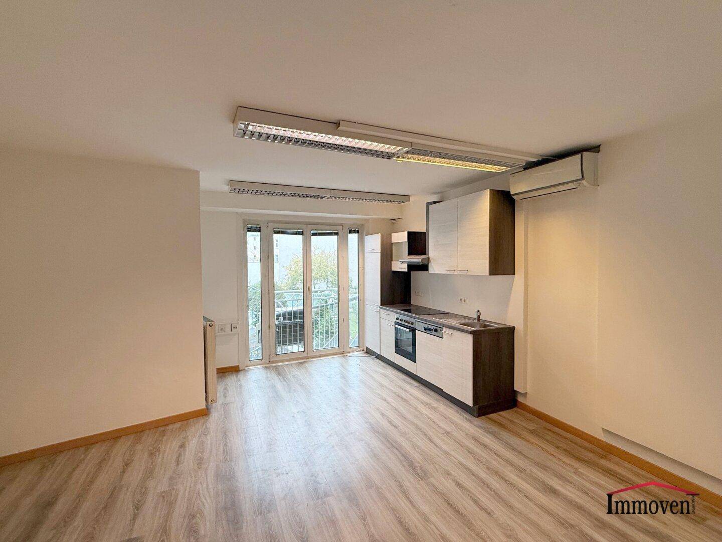 Offener Wohnbereich mit integrierter Küchenzeile und Zugang zum Balkon.