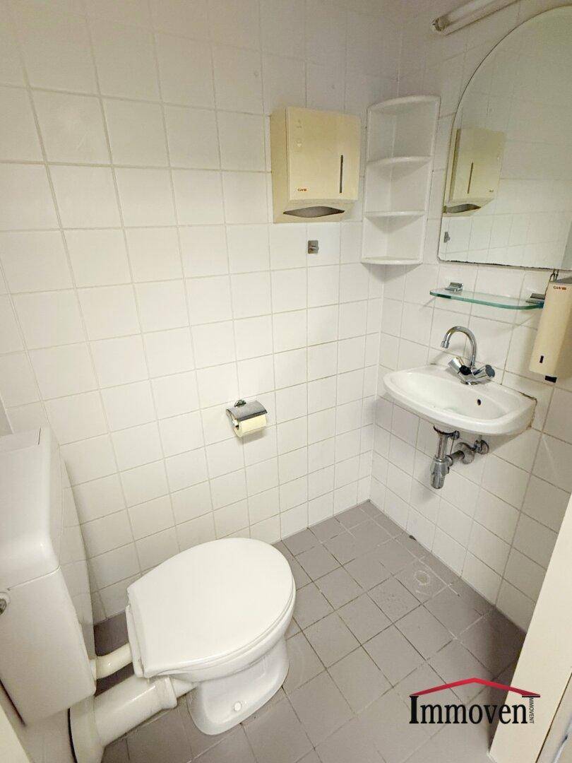Kleines WC mit Toilette, Waschbecken und weißen Fliesen.