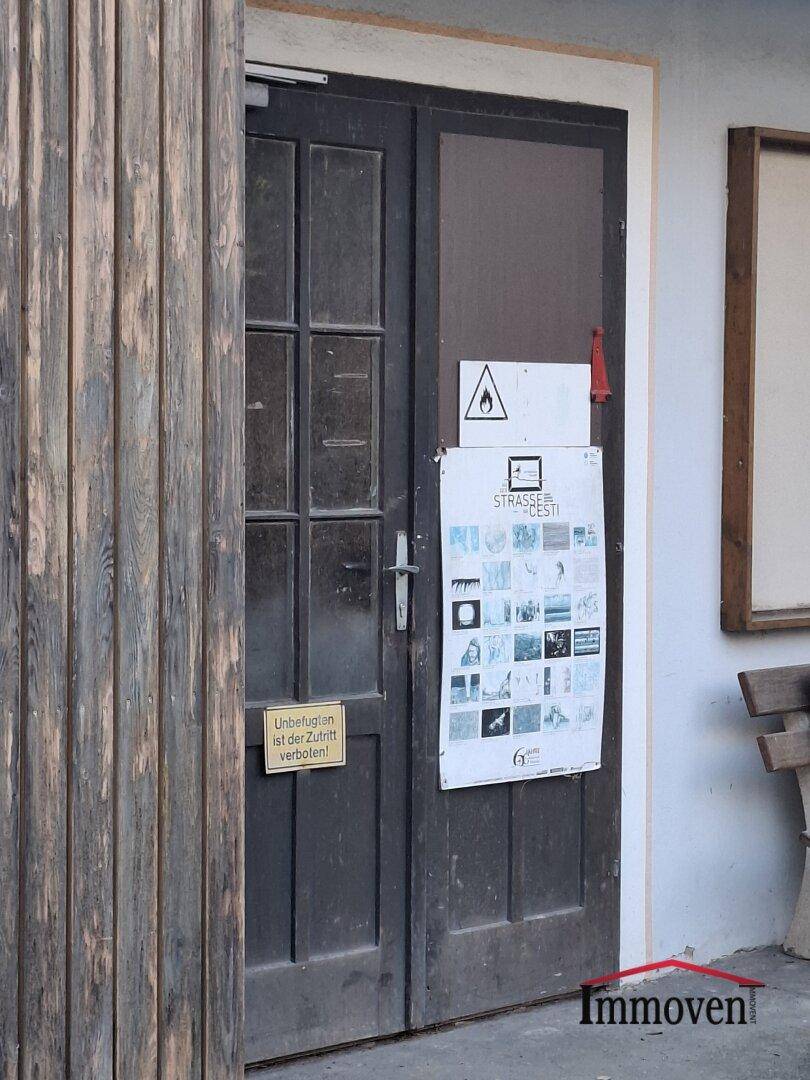Eine dunkle Holztür mit Glasfeldern und mehreren angebrachten Schildern, darunter ein Warnhinweis.
