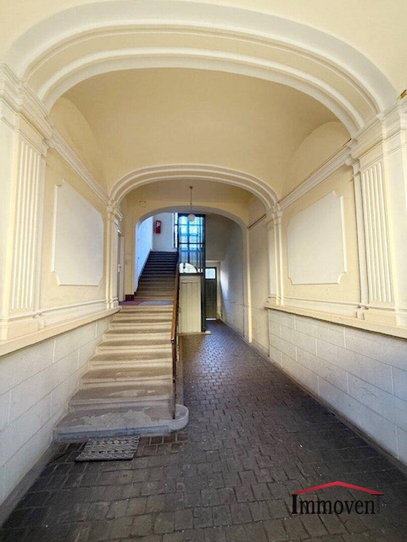 Eindrucksvoller Eingangsbereich eines Altbaus mit hoher Gewölbedecke, Stuckverzierungen und Steintreppe.
