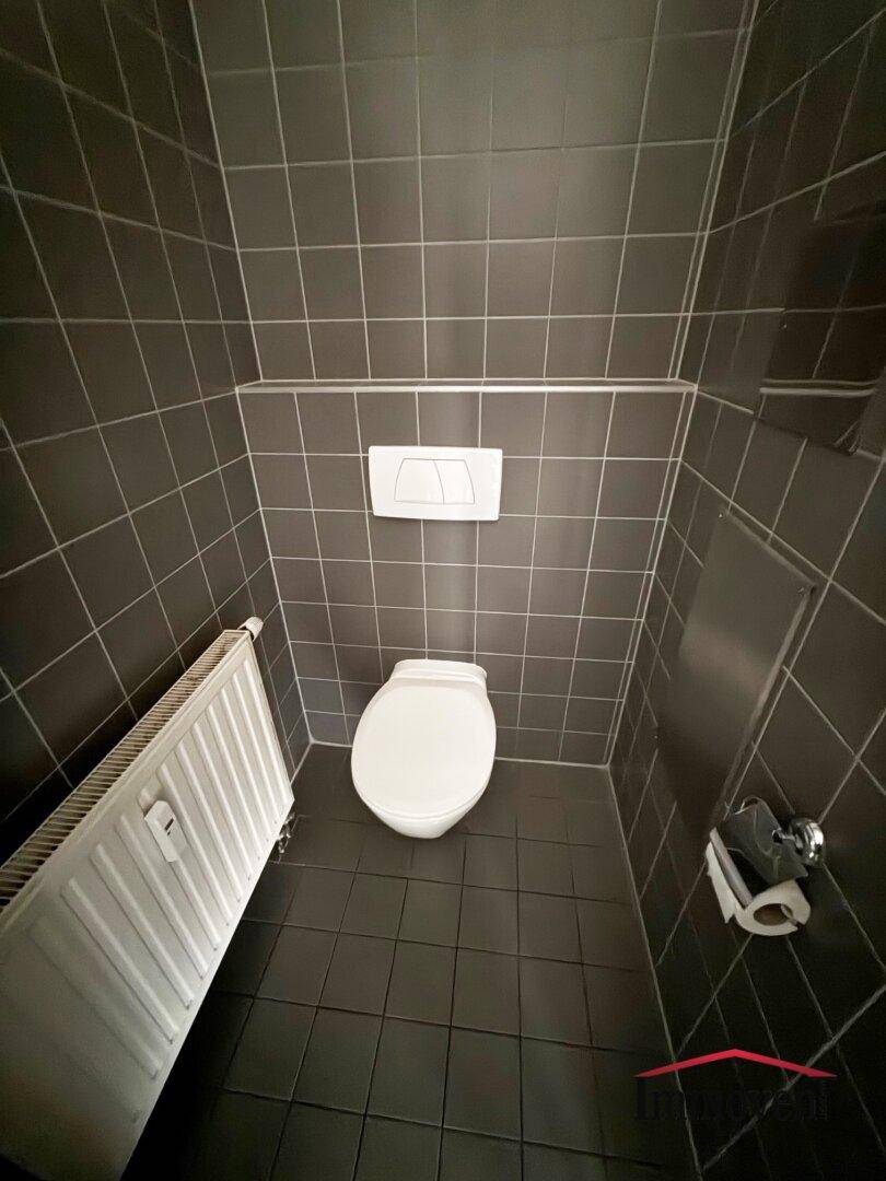WC-Kabine mit dunklen Fliesen, Heizkörper und weißer Toilette, bietet eine saubere und funktionale Ausstattung.