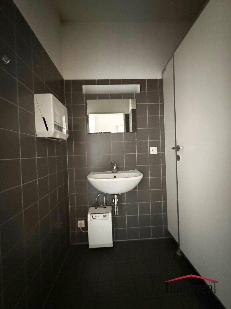 Modern gefliestes WC mit Waschbecken, Spiegel und dunklen Fliesen, in gutem und gepflegtem Zustand.
