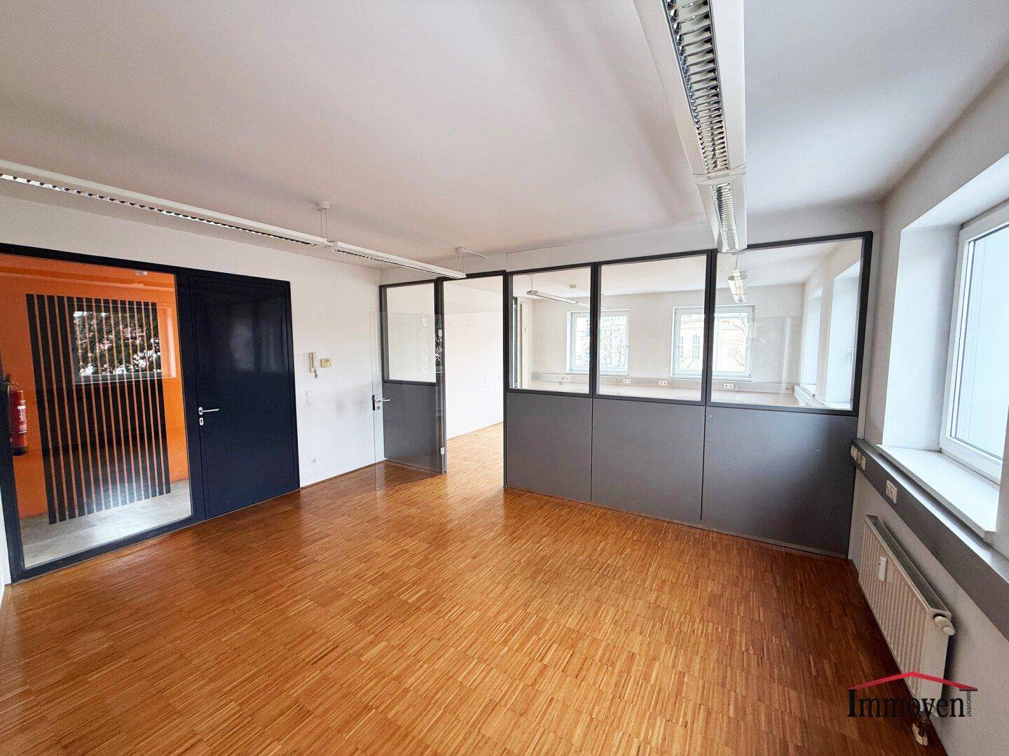 Büroraum mit Holzparkett, Glaswänden und Zugang zu weiteren Räumen, bietet eine moderne Arbeitsumgebung.