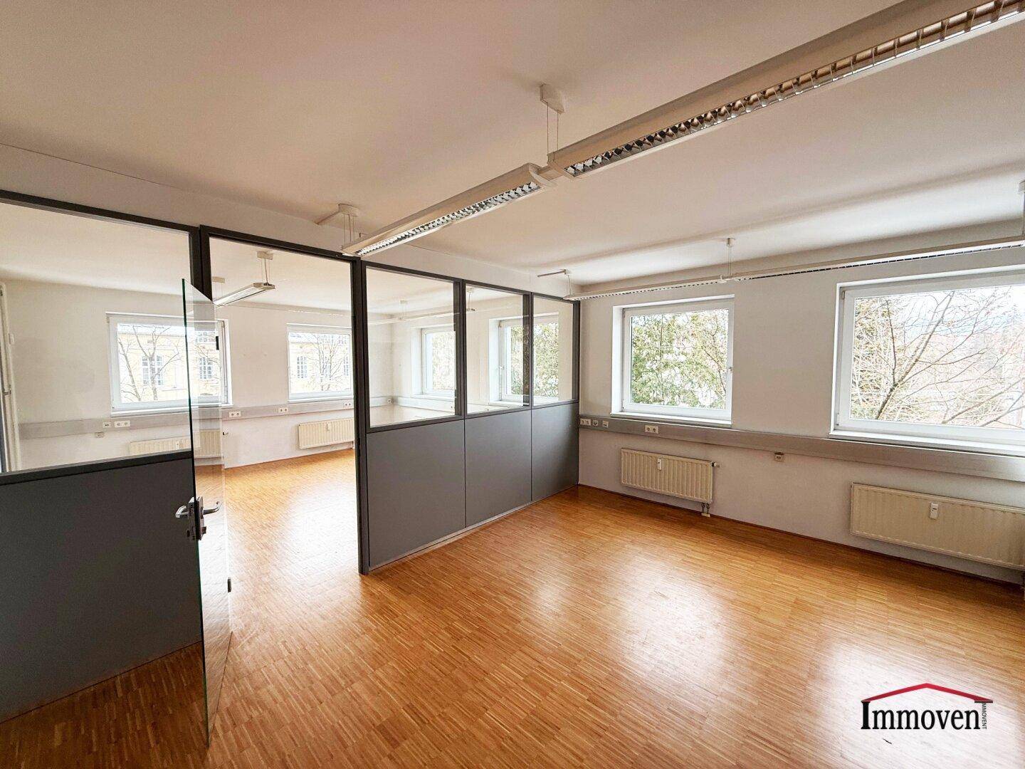 Heller Büroraum mit Holzparkett, Glaswänden und Blick ins Grüne, ideal für offene Bürokonzepte.
