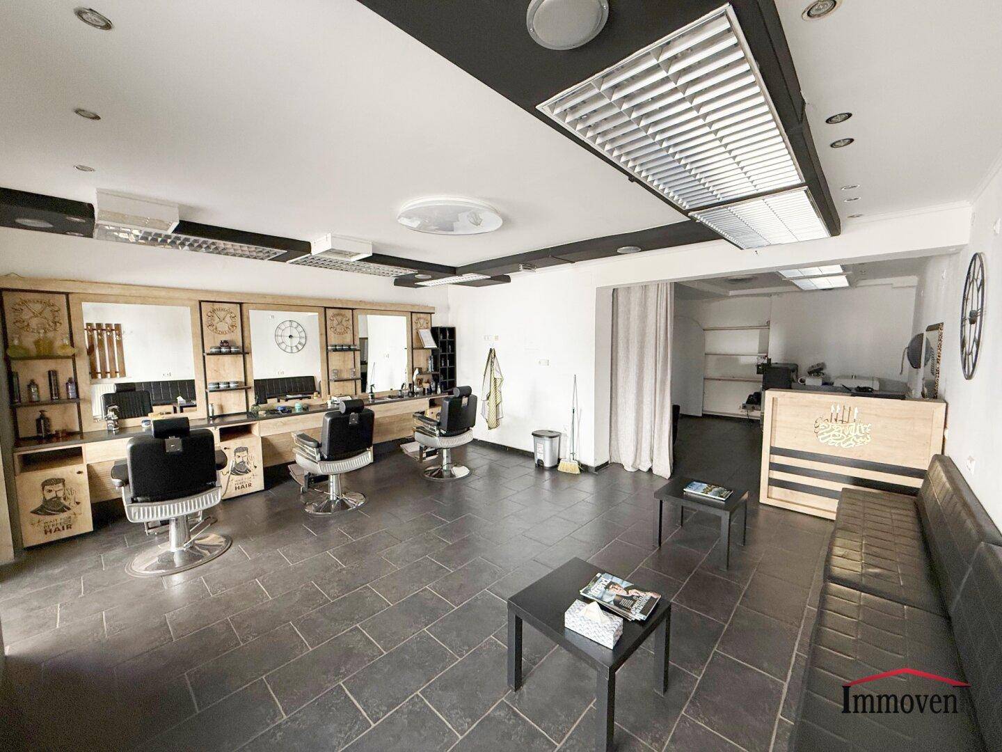 Heller Friseursalon mit mehreren Arbeitsplätzen, Spiegeln und einem Durchgang zu einem hinteren Bereich.