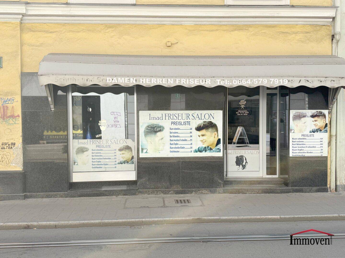 Außenansicht eines Friseursalons mit Schaufenstern und Markise an einer belebten Straße.