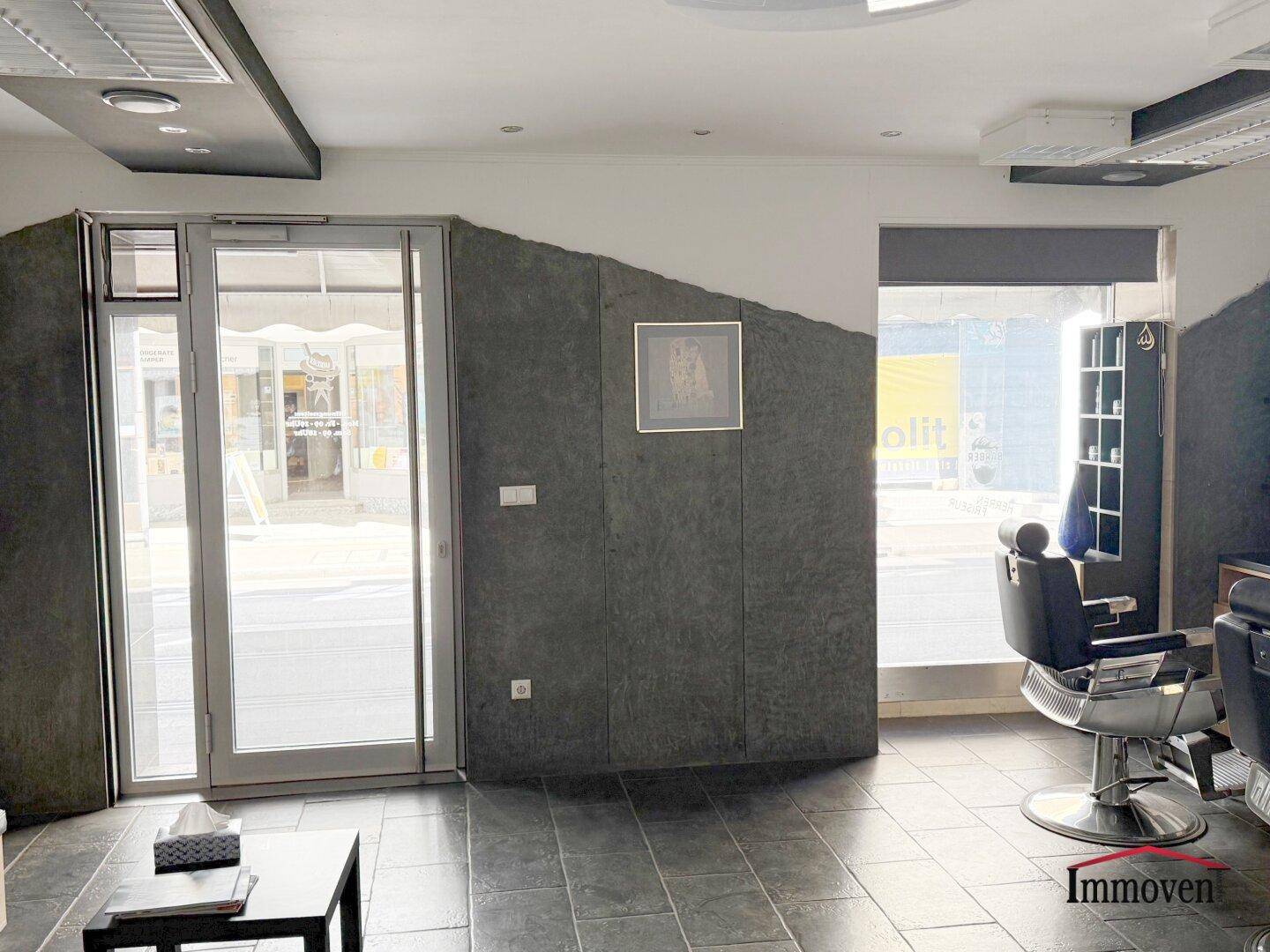 Eingangsbereich eines Friseursalons mit großer Glastür und Schaufenster, das viel Tageslicht hereinlässt.