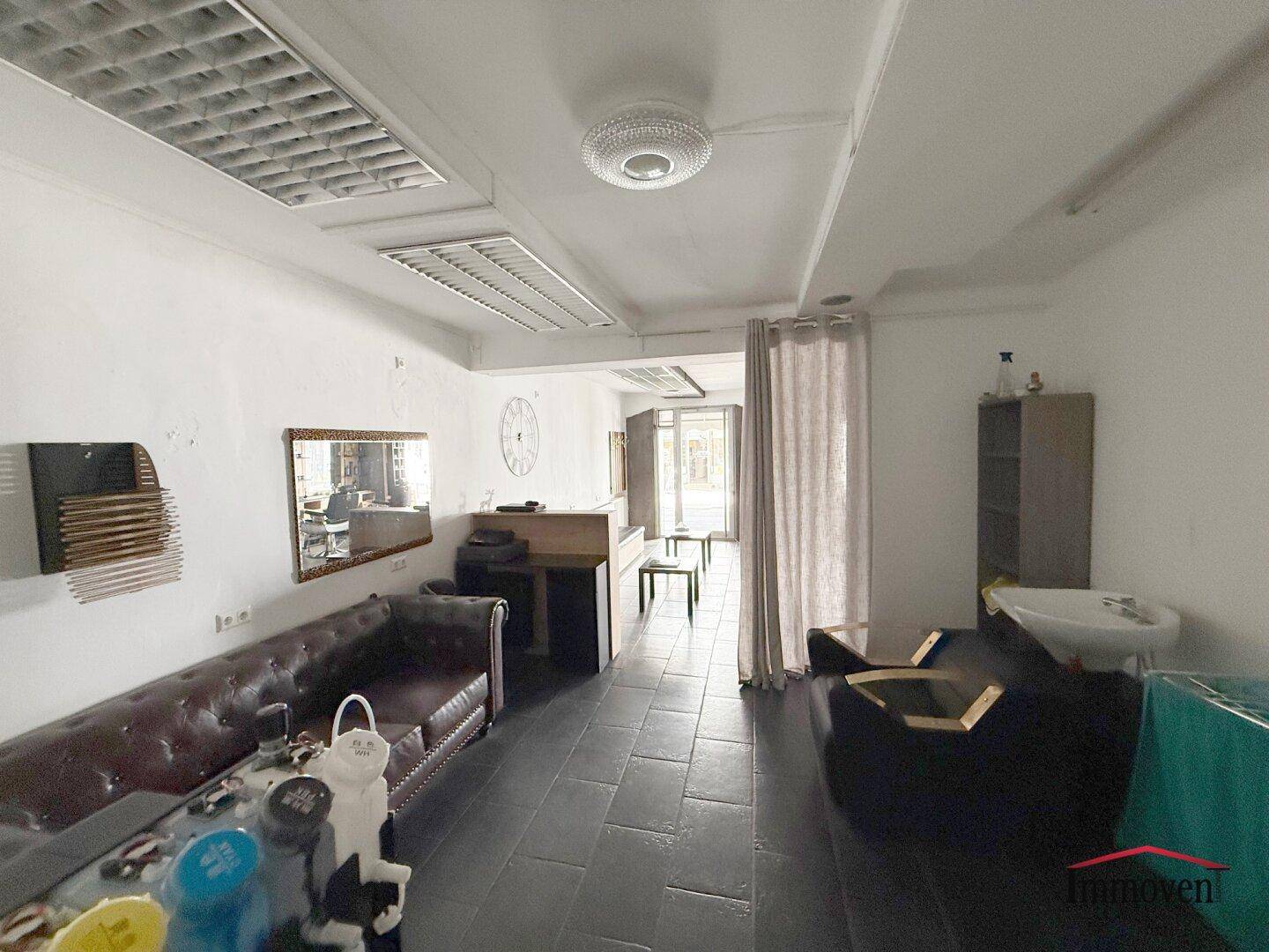 Hinterer Bereich des Salons mit Ledersofa, Waschbecken und einem Vorhang, der einen weiteren Raum abtrennt.