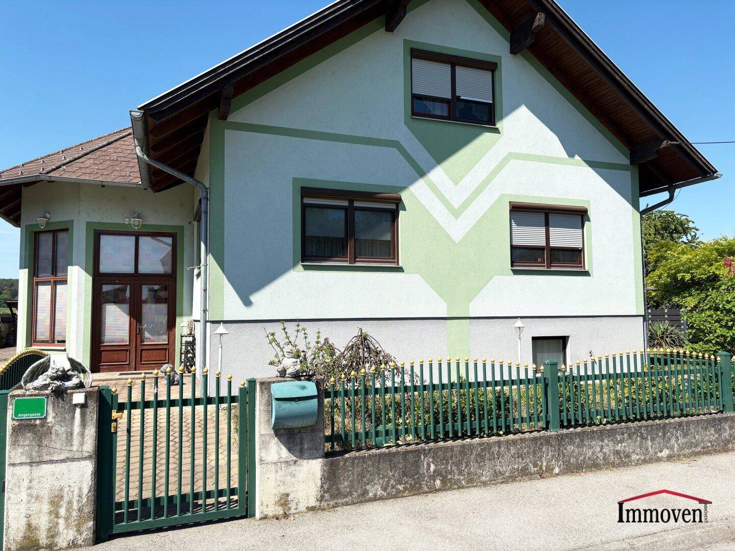 Nahaufnahme der Hausfassade mit grünem Zaun, Briefkasten und dekorativen Mustern.