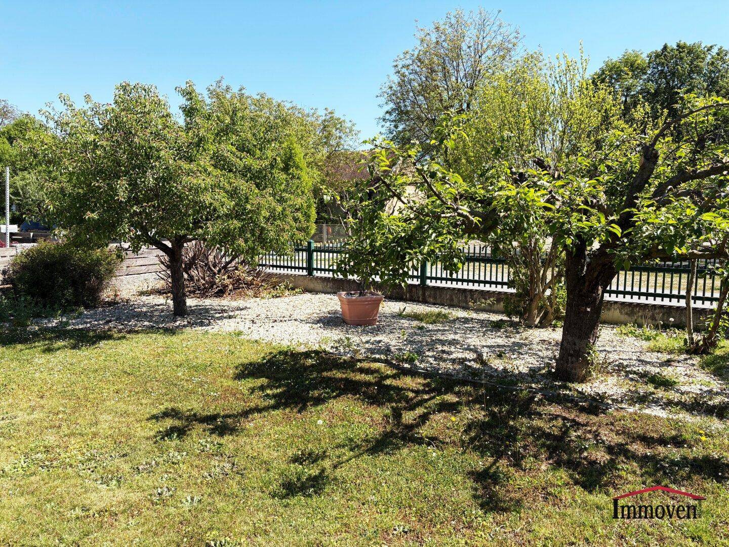 Naturbelassener Gartenbereich mit Obstbäumen, Kiesflächen und einem Zaun im Hintergrund.